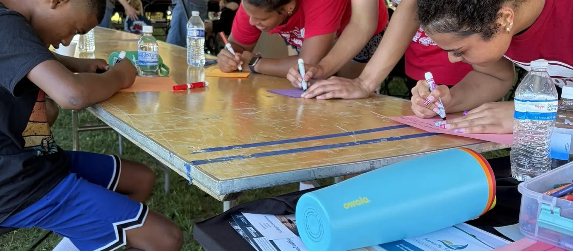 Teenagers making cards at a folding table under a tent