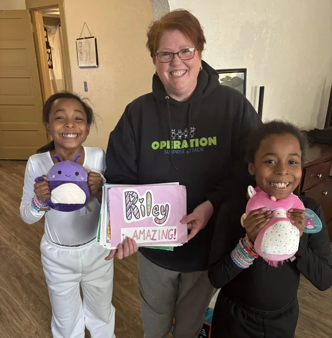 Two sisters holding a handmade card and plush toys